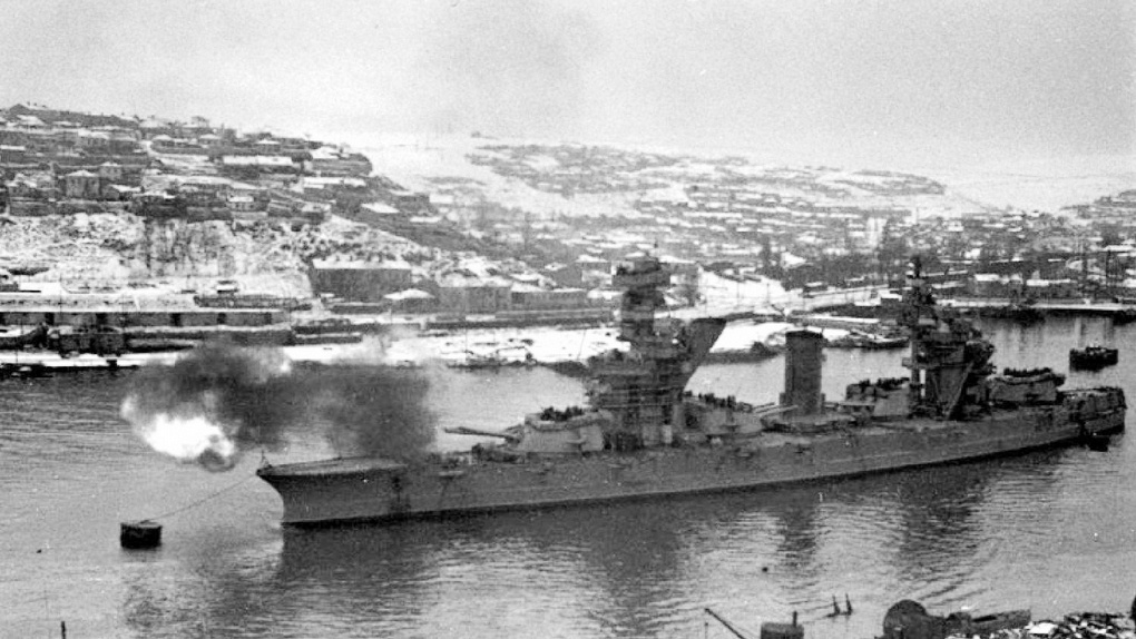 Линкор «Севастополь» ведёт огонь по врагу со стоянки в бухте.