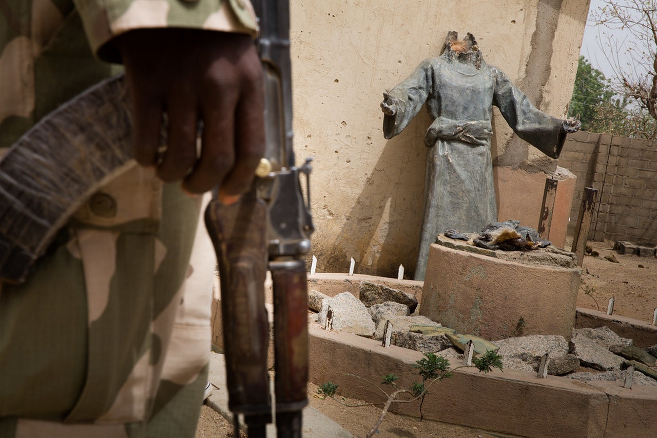 Солдат армии Нигерии стоит перед статуей Святого Патрика на территории католической церкви после освобождения территории от исламистских террористов, 2015 г.