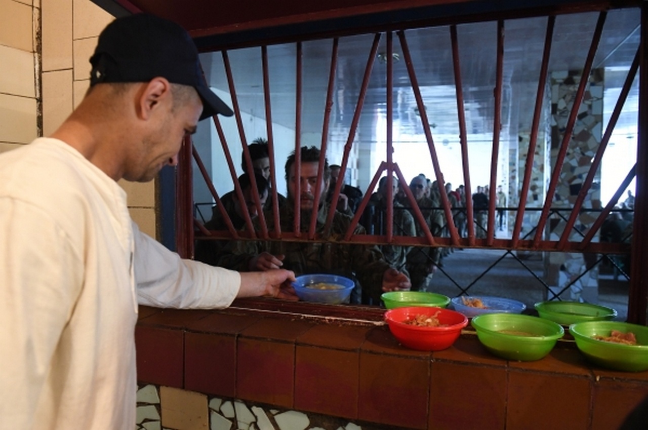 Украинские военнопленные стоят в очереди за едой в столовой исправительного учреждения.